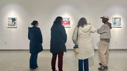 Zoom image: Joel Mulindwa speaking with visitors in Project Space gallery, for exhibition "Impressions of Gratuity", featuring his oil pastel drawings of tip jars.