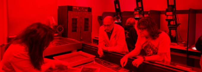 Zoom image: three people around water baths and trays in a photoigraphy daerk room