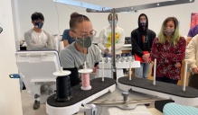 Leanne Goldblatt demonstrates how to thread the embroidery machine to a group of students.