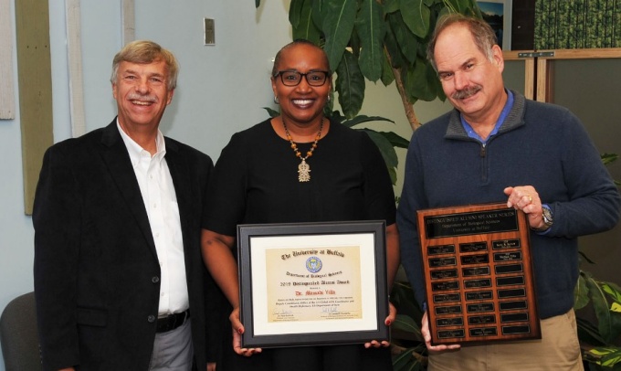 Dr. Mamadi Yilla (center) receives the 2019 Distinguished Alumni Award from Dr. Gerald Koudelka, Associate Dean for Research (left), and Dr. Paul Gollnick, Professor and Chair, Department of Biological Sciences (right). Dr. Yilla serves as deputy coordinator for multi-sector responsibility and diplomacy in the Office of the U.S. Global AIDS Coordinator and Health Diplomacy (S/GAC). Photograph by Jim Stamos. 