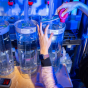 A student researcher works at a biology lab bench, adjusting clear cylindrical water tanks connected by tubing while conducting research on fish eggs using AI-assisted analysis. 