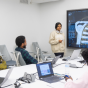 Students sit around a conference table with laptops while an instructor presents a 3D anatomical visualization of the human torso and nervous system on a large digital display during a cellular signaling class. 
