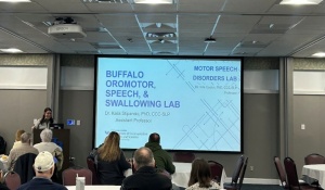 Prof. Kaila Stipancic presents research from the Buffalo Oromotor, Speech & Swallowing Lab to attendees seated at tables at Parkinson&rsquo;s Awareness Day. 