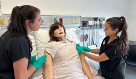 UB SLP Students Megan Orrange and Alli Barsi prepare an airway mannikin for a speaking valve trial in a simulated hospital room. 