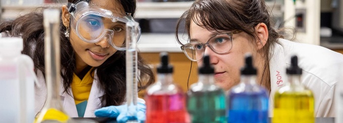 High school and PhD student examine their alginic acid experiment with droppers and lab equipment in front of them. 