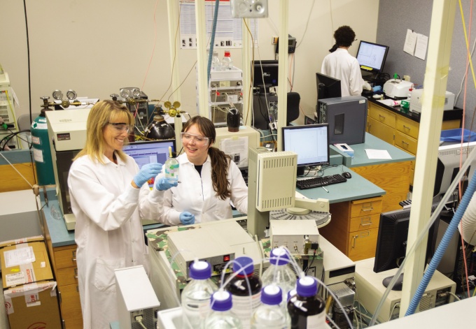 Lab center featuring two people in white lab coats, one holding a beaker. 