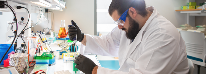 PhD student working in a research lab, holding a pipette. 