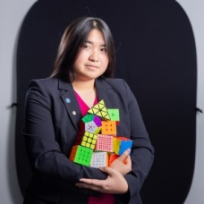 Lauren Phung holding 10 different types of rubik's cubes. 
