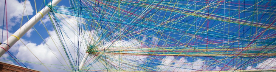 Different colored strings attached to multiple poles set up outside under a cloudy blue sky. 
