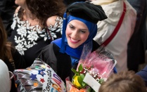 Graduating student holding a "congrats grad" balloon and bouquet of flowers. 