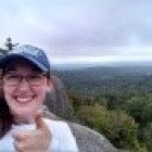 Katie Lovell standing on a mountain with a backdrop of green vegetation. 