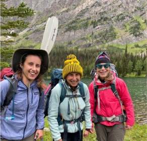 Sarah Wensink, Gabby Feber and Richelle Allen-King standing by a lake with a gorgeous view of trees and a mountain in the background. 