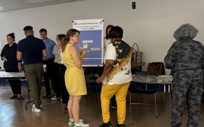 Kelly standing in fron t of a poster engaged with the community. 