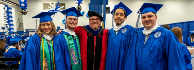 A group of students with a professor at commencement. 