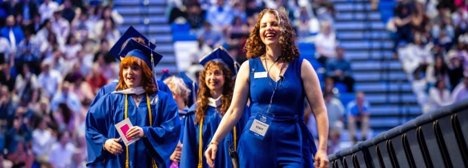 staff member leading a line of students at commencement. 