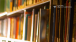 Zoom image: A closeup of books in the library with the College of Arts and Sciences logo.