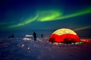 A view of the northern lights of the aurora borealis swirling above the ice sheet, lime green in a dark, lonely sky. 