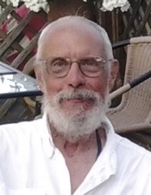 Rossman Geise, headshot outside on a patio. He is wearing eyeglasses and has a gray beard. 