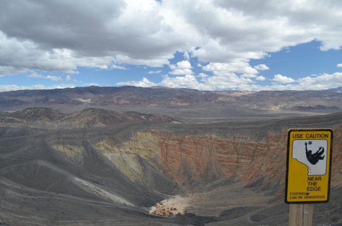 A view across Ubehebe crater that shows a small playa (dry lake bed) at the bottom of the crater. The orange and yellow layered rocks show the pre-eruption “bedrock”. These are draped by gray ejecta deposits. 