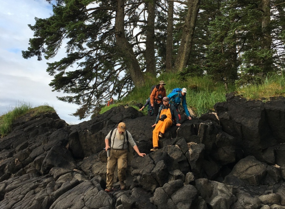 A group carefully climbing down a rock path with forest trees in the background. 