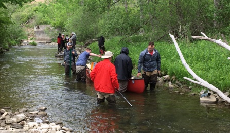 Field camp students are working in a low part of a creek. They are wearing waterproof clothing while they use instruments to check on the water. 