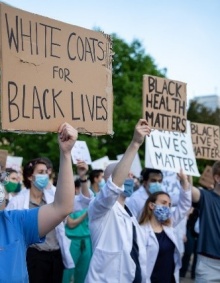 Medical students protesting and holding signs saying, "white coats for black lives", "black health matters" and "black lives matter". 