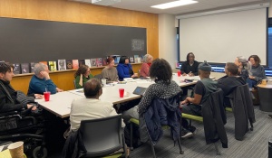 Photo of people seated around a conference table engaged in conversation with presenter Rinaldo Walcott. 