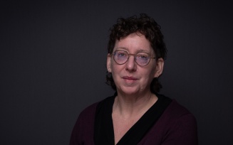 Photo portrait of Alexis Shotwell, wearing glasses with a dark shirt on dark background, with a serious expression. 