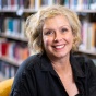 Photograph of Elizabeth Mazzolini seated in an armchair in front of shelves filled with books. 