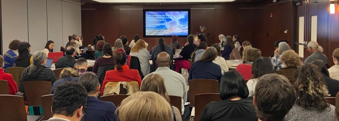 Audience viewing presentation with speaker in background. 