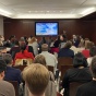 Audience viewing presentation with speaker in background. 