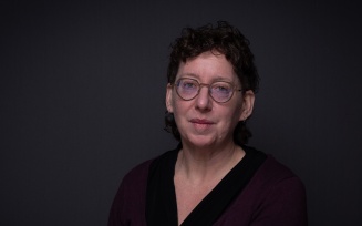 Photo portrait of Alexis Shotwell, wearing glasses with a dark shirt on dark background, with a serious expression.