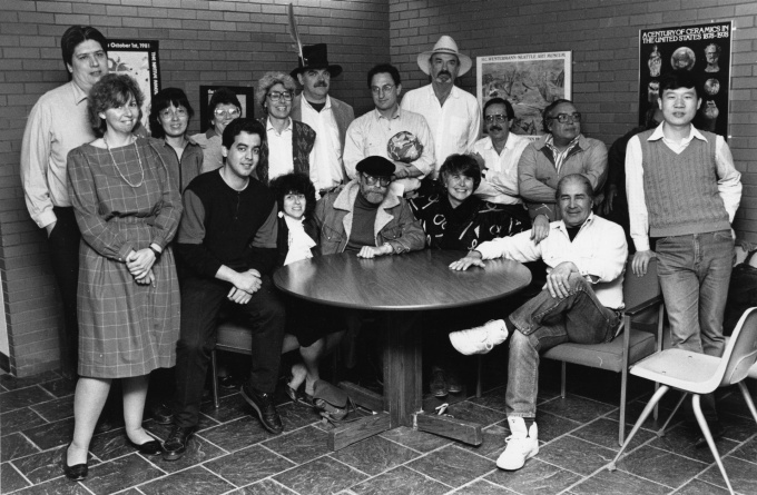 Group of sixteen people standing or sitting around a table in a hallway. K.C. Kratt; American Studies faculty, 1987; 24.4x16cm; Copyright 1987 University at Buffalo. 