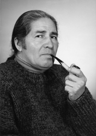 A man looking at a camera, holding a pipe at his mouth. American Studies professor Oren Lyons, 1978; 11.9x16.8cm; Copyright 1978 University at Buffalo. 