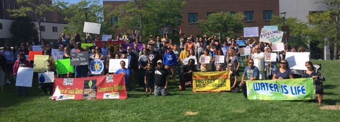 Large group of students and faculty with signs of support, on a green lawn. 