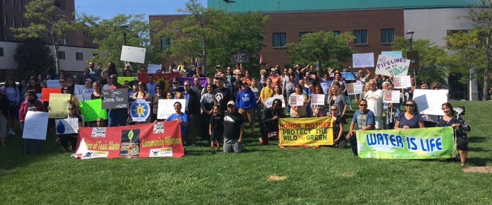 Large group of students and faculty with signs of support, on a green lawn. 