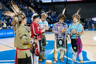 Zoom image: Five men as a part of the Indigenous Spirit Dancers performing at the Native American Heritage Night during halftime of the Mens Basketball game
