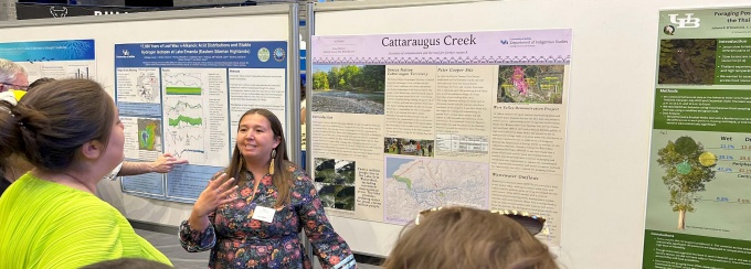 A student standing in front of a research poster speaking with three individuals about her project. 