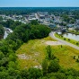 Drone image over an outdoor space. Green grass, trees, a road, water, and buildings are visible in this image. 