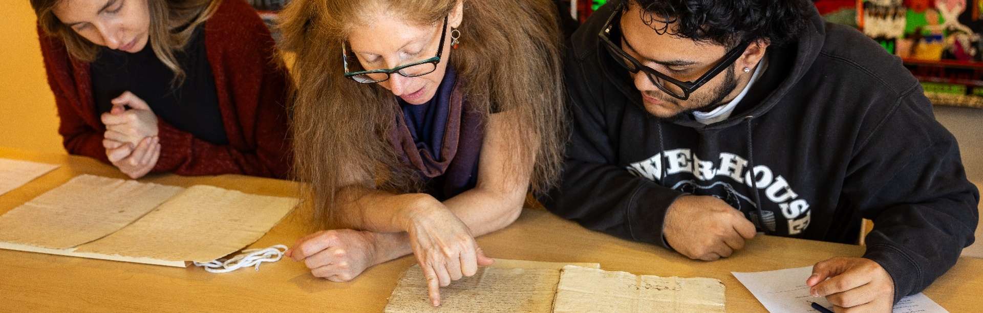 Students examine rare books and manuscripts during a University Libraries Special Collections visit, with an instructor pointing out details on a historical document. 