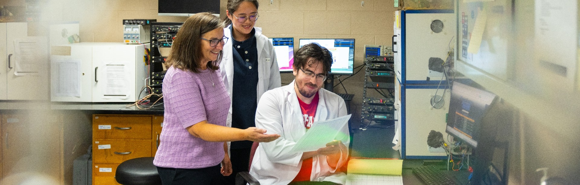 Professor Michael Dent works with two students reviewing research data in a psychology lab studying how humans and animals perceive and respond to sound. 