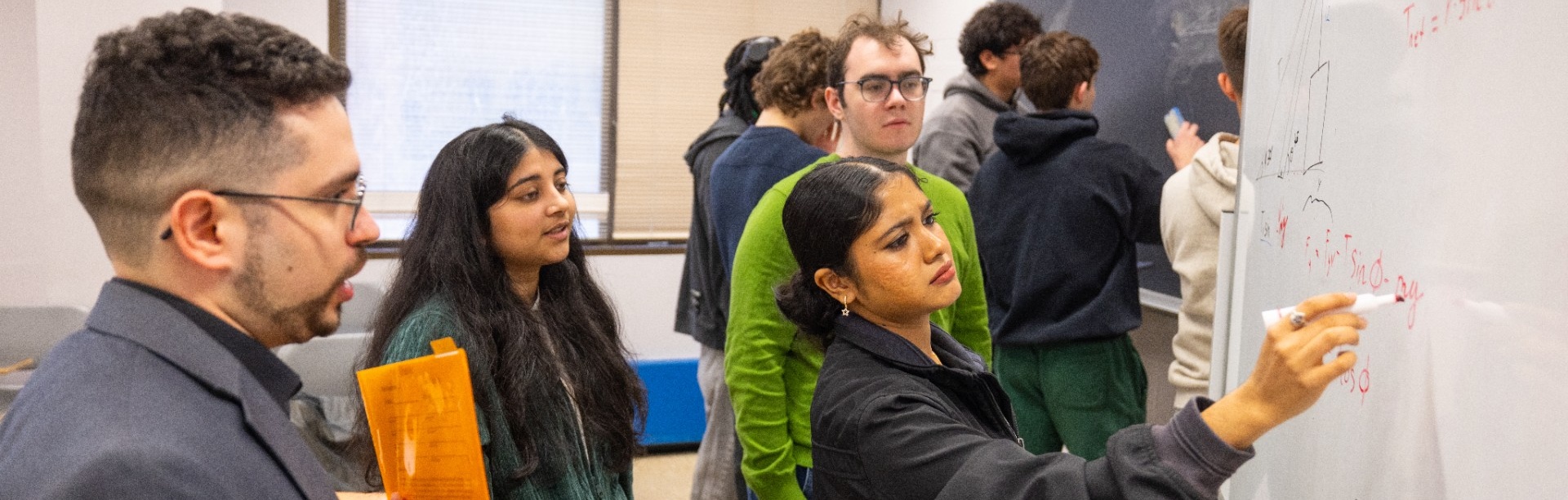 Students solve physics problems together at whiteboards in an active learning classroom. 