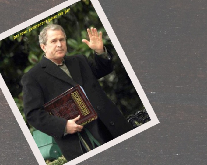 George Bush carrying the Schottenstein Talmud in his right hand while waving out with his left. He is wearing a long gray coat and this picture is sitting on top of a desktop. Above George Bush's head is a yellow line of text that reads:. 