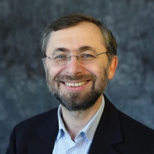 Sergey Dolgopolski wearing blue pin stripe shirt and black suit jacket. He has a mustache and beard and wearing frameless eyeglasses. 