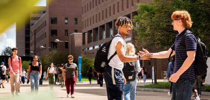 Two students greet each other on a busy UB north campus walkway. 