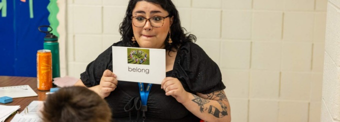 A woman holds up a card with the word &ldquo;belong&rdquo; while working with a child in a classroom. 