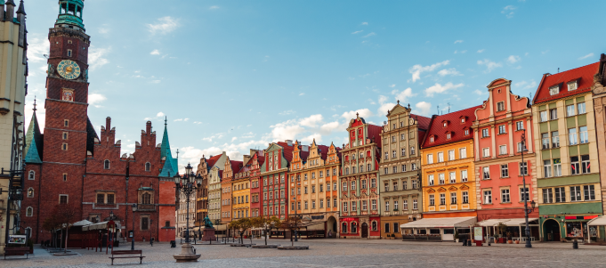 Colorful historic buildings and a clock tower border a cobblestone square in Wrocław, Poland. 