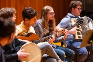 musicians playing guitars, drum and accordion in a circle. 