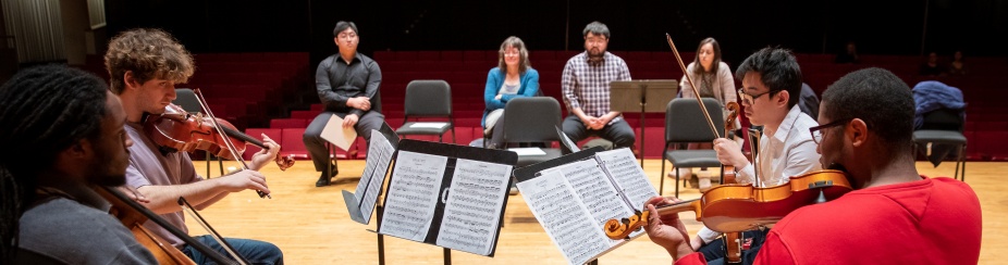 Musicians playing on stage in front of faculty and students. 