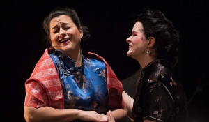 Two opera singers performing on stage holding hands. 